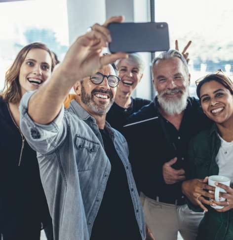 A group of happy company employees of various ages taking a group selfie